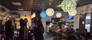 A busy night at Hava Kava Stuart: guests at the bar and around a card table, under glowing flower-shaped pendant lights